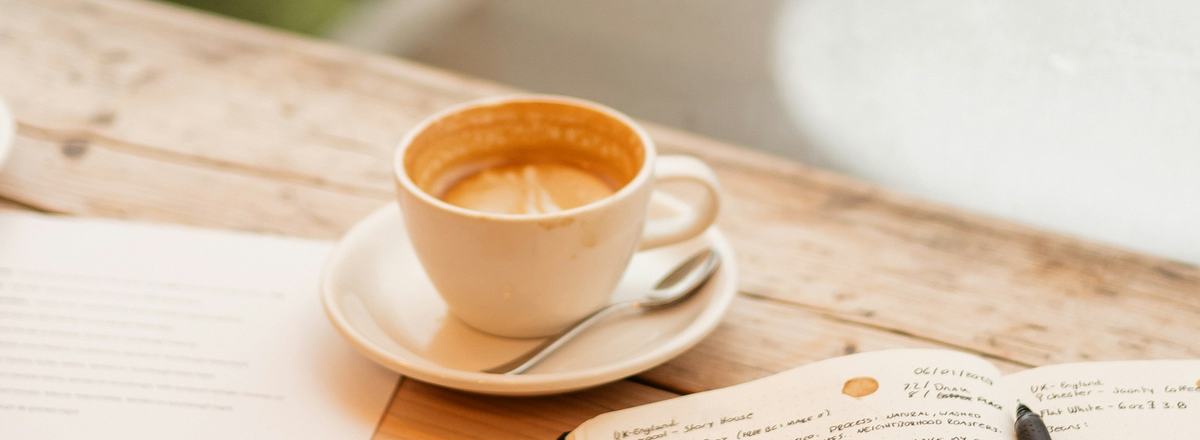 A cup of coffee and an open notebook on a wooden table